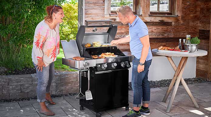 Husband and wife laughing together at the grill while husband turns meat on the grill grate.