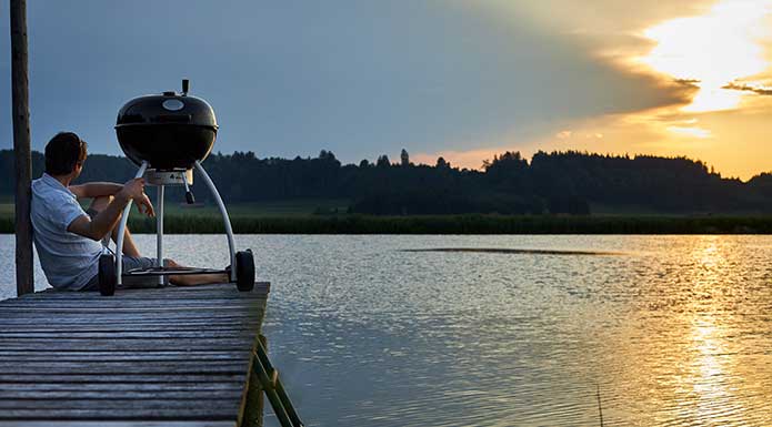 Holzkohle Kugelgrill auf Steg mit Sonnenuntergang