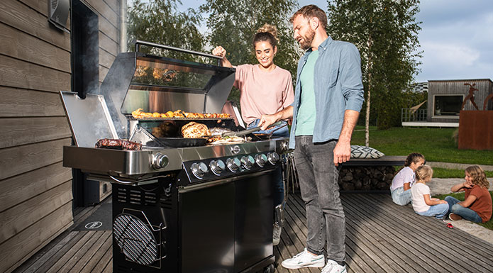Gas barbecues Couple standing at the barbecue. Man turns meat and woman watches