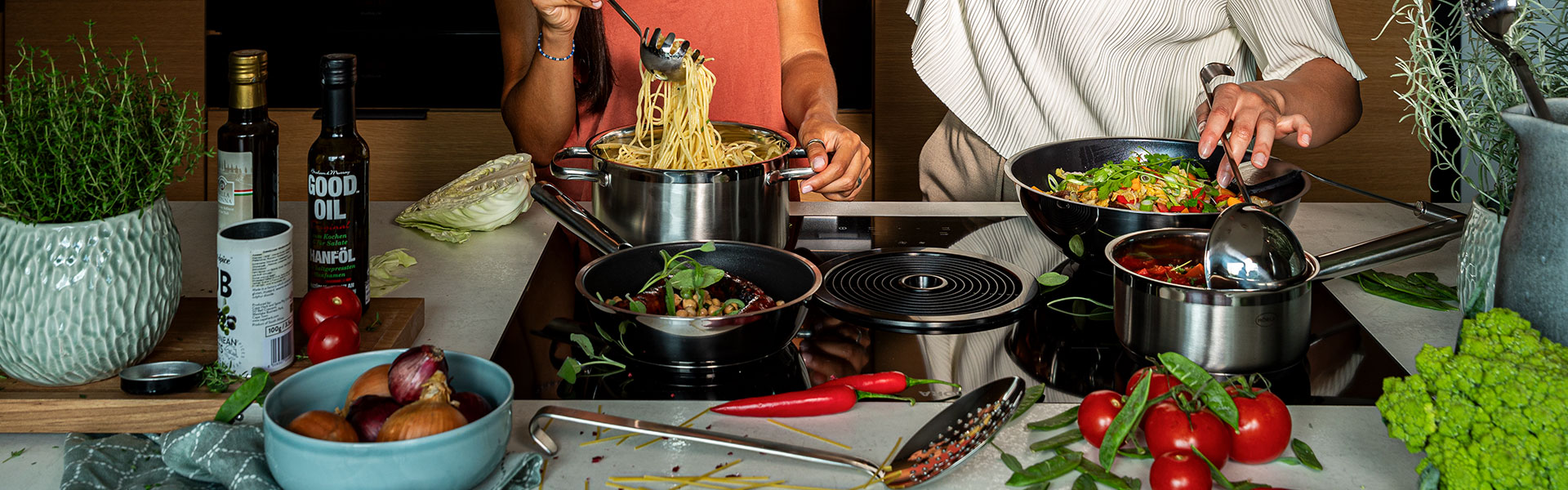 Zubereitung von Gerichten mit RÖSLE Kochgeschirr Zwei Personen bereiten verschiedene Gerichte in Kochgeschirr auf einer modernen Kochplatte...