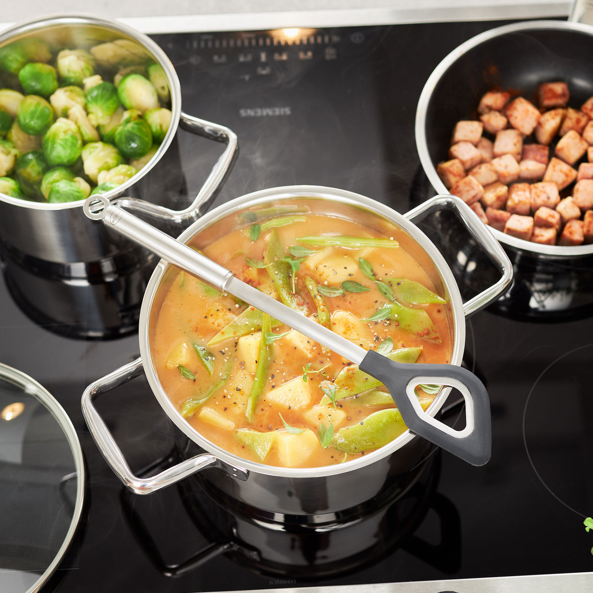 RÖSLE Kochtopf Set mit Gemüse Kochtopf mit Gemüsebrühe und Gemüse, daneben zwei weitere Töpfe mit Rosenkohl und angebratenem...
