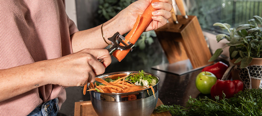 Header storage Woman peeling carrots in a stainless steel bowl with the Rösle pendulum peeler crosswise.