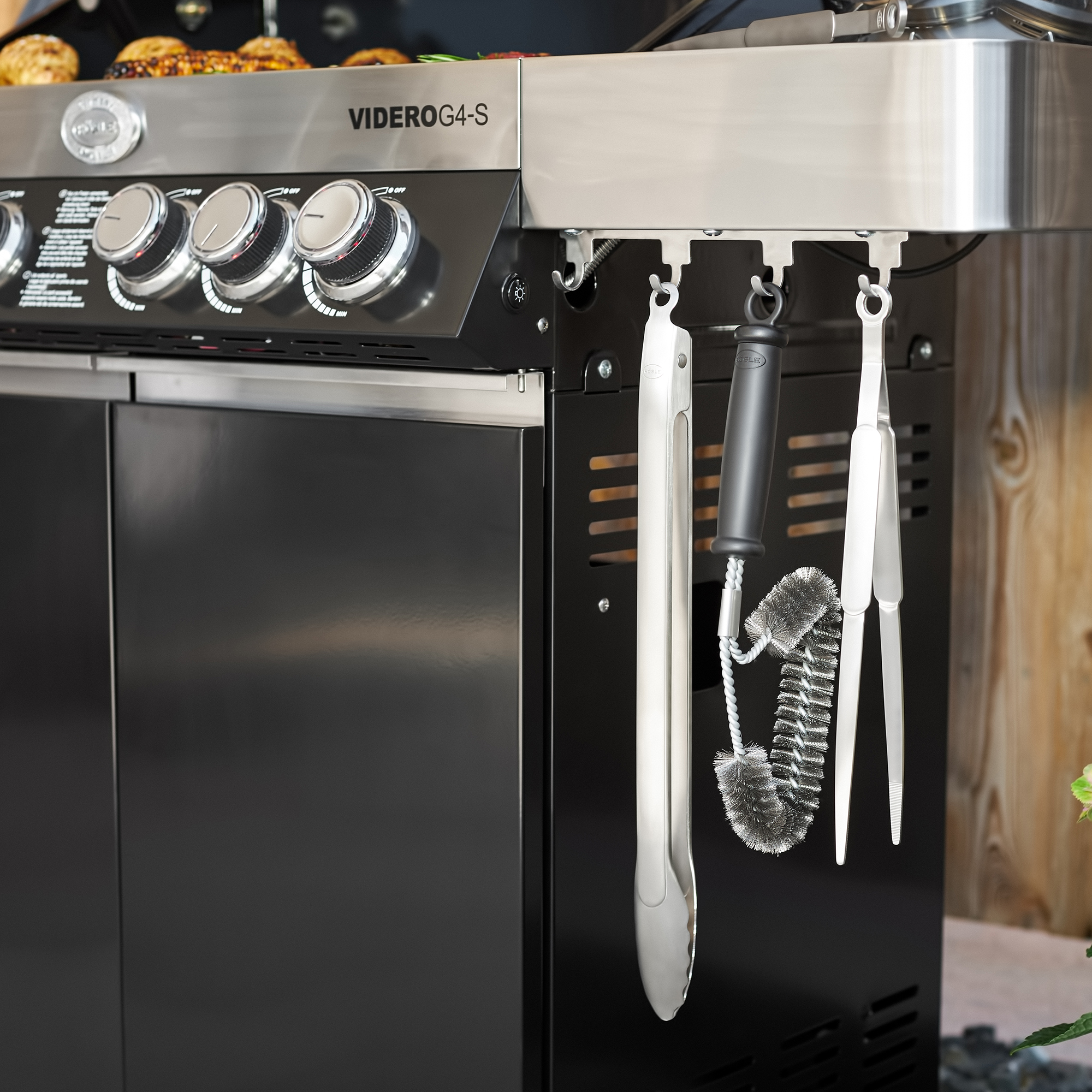 RÖSLE needle nose tongs and barbecue tools Stainless steel pointed tongs, hanging from a barbecue, next to barbecue tools such as a barbecue...