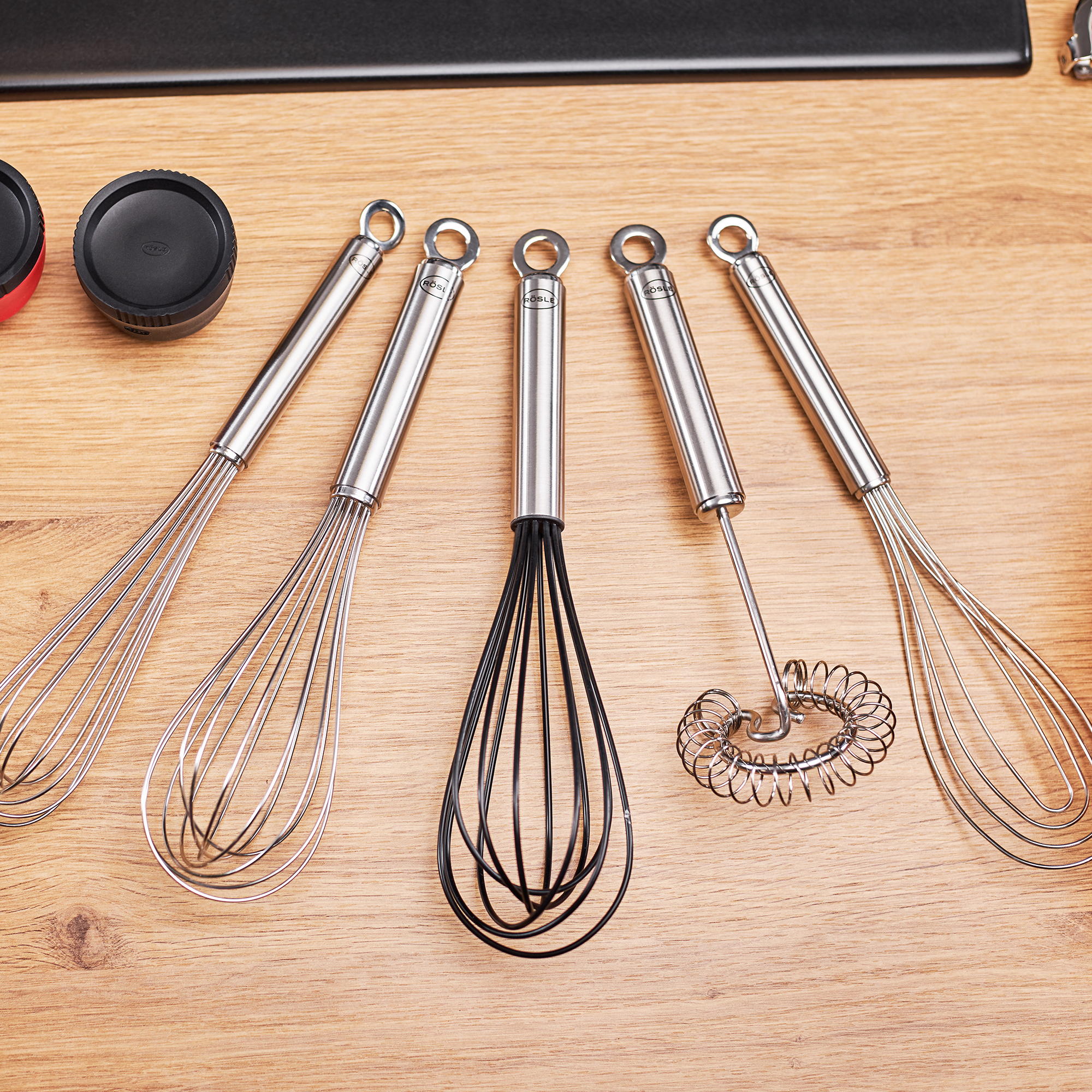 RÖSLE spiral whisk and stainless steel whisk Spiral whisk in black and four other stainless steel whisks on a wooden base.