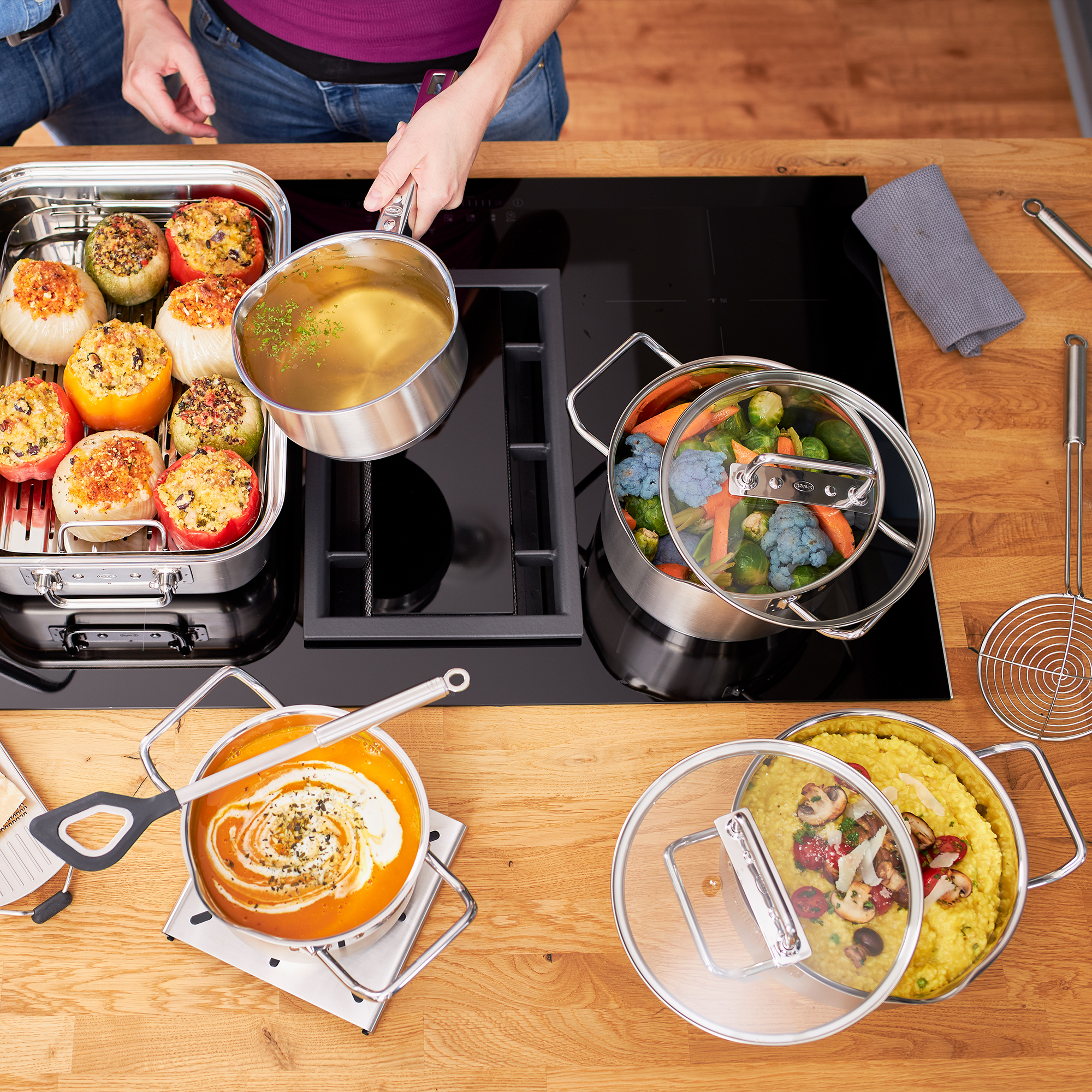 RÖSLE Topfset auf Kochfeld Topfset, vier Teile, auf einem Kochfeld mit gefüllten Paprika, Gemüse und einer Suppe.