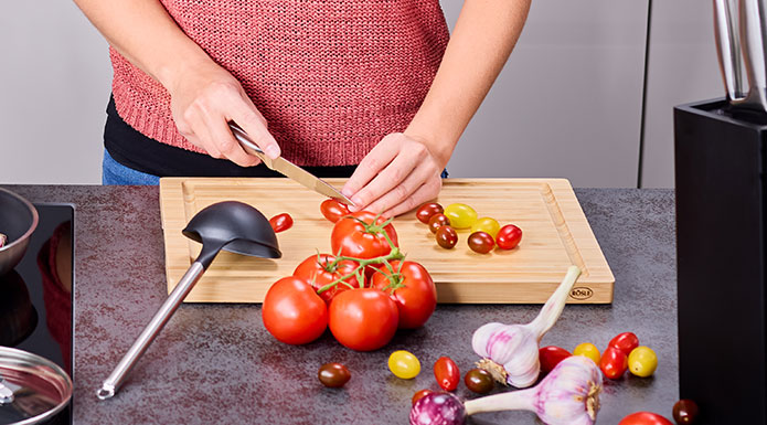 Woman cuts tomatoes with knife on cutting board