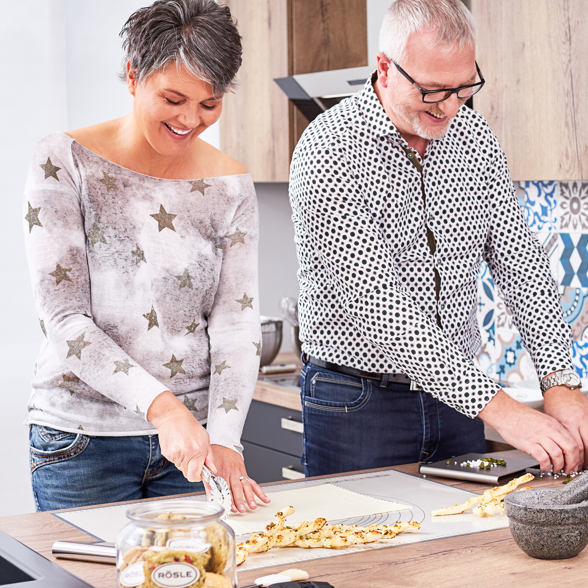 Two people rolling out the dough Two people are preparing dough on a work surface, a woman in a grey star top and a man in...