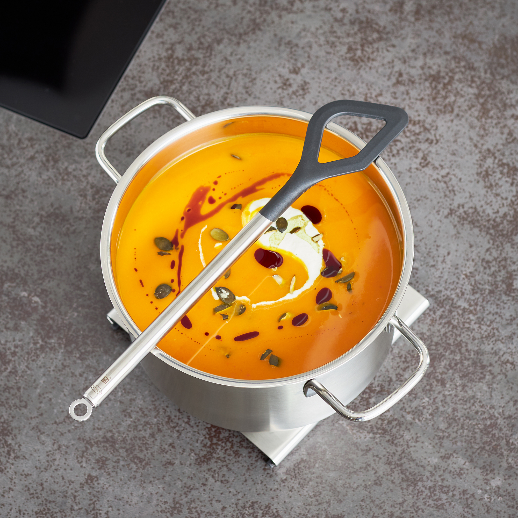 RÖSLE Kochlöffel 32 cm in einem Topf mit Suppe Kochlöffel aus Edelstahl, 32 cm, mit grauem Griff, in einem Topf mit orangefarbener Suppe.