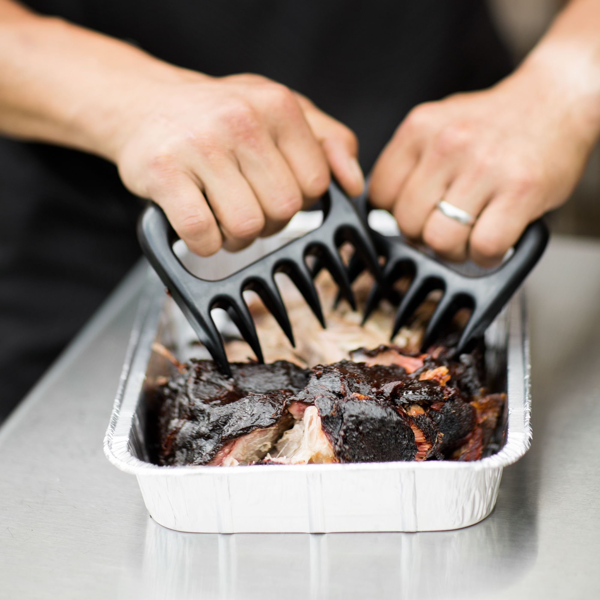 RÖSLE Pulled Pork Gabeln Pulled Pork Gabeln in Schwarz, verwendet zum Zerkleinern von Fleisch in einer Aluschale.