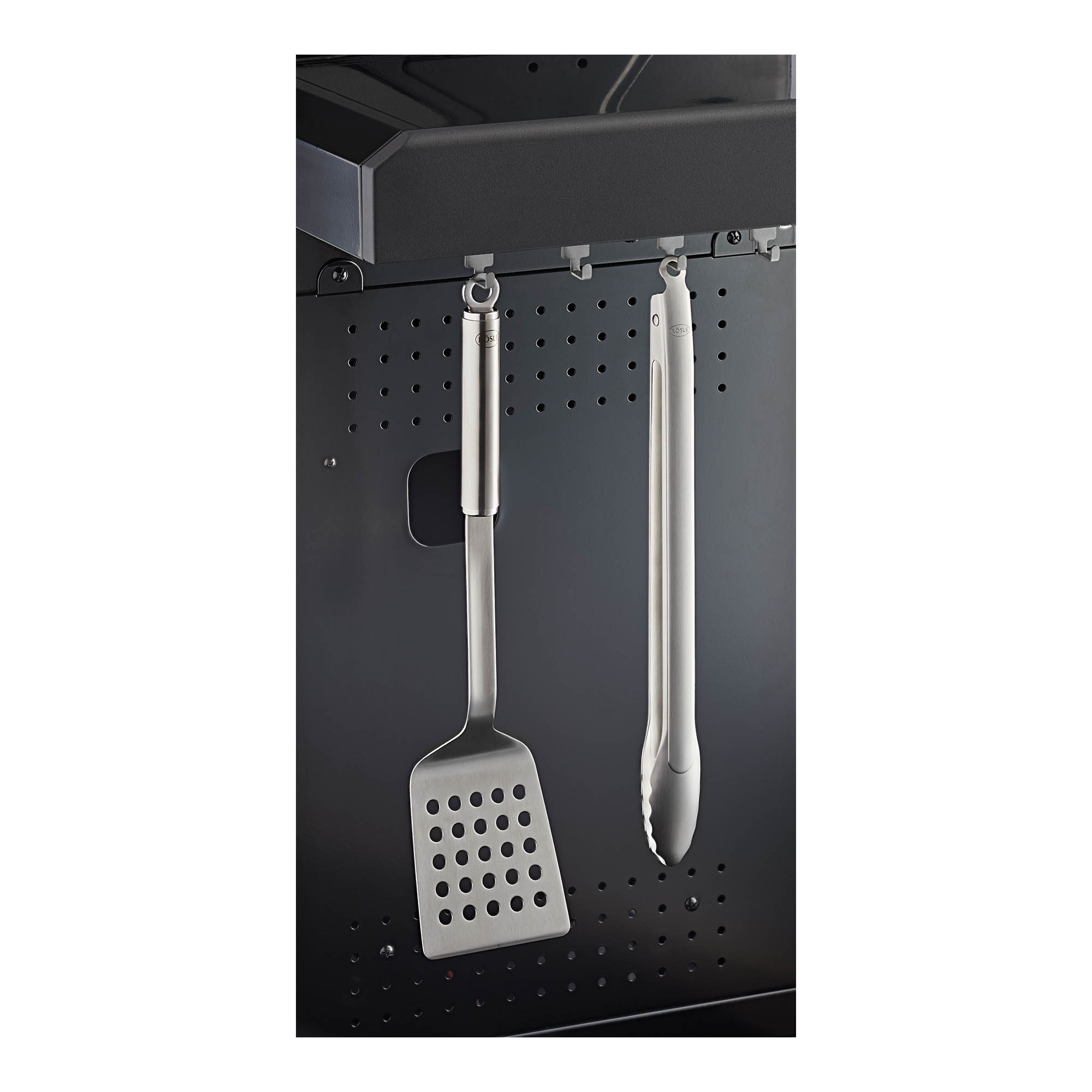 RÖSLE Grillzubehör aus Edelstahl Grillzubehör: Edelstahl Wender und Zange hängen an einem schwarzen Grill.