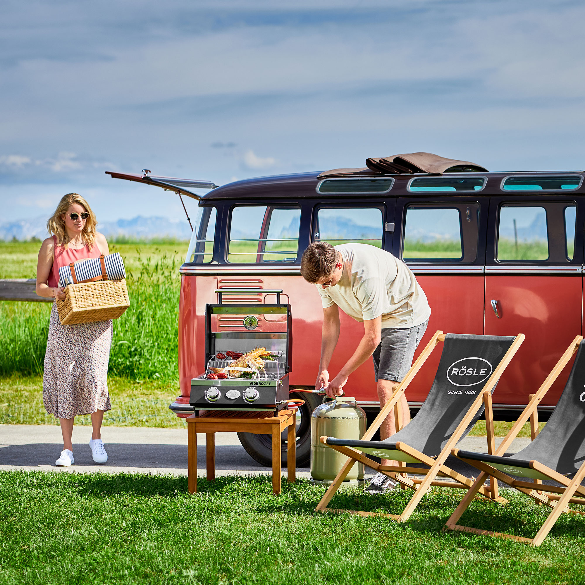 RÖSLE Videro G2-P Grill im Freien Videro G2-P Grill auf einem Tisch, während eine Frau mit einem Korb steht und ein Mann am...
