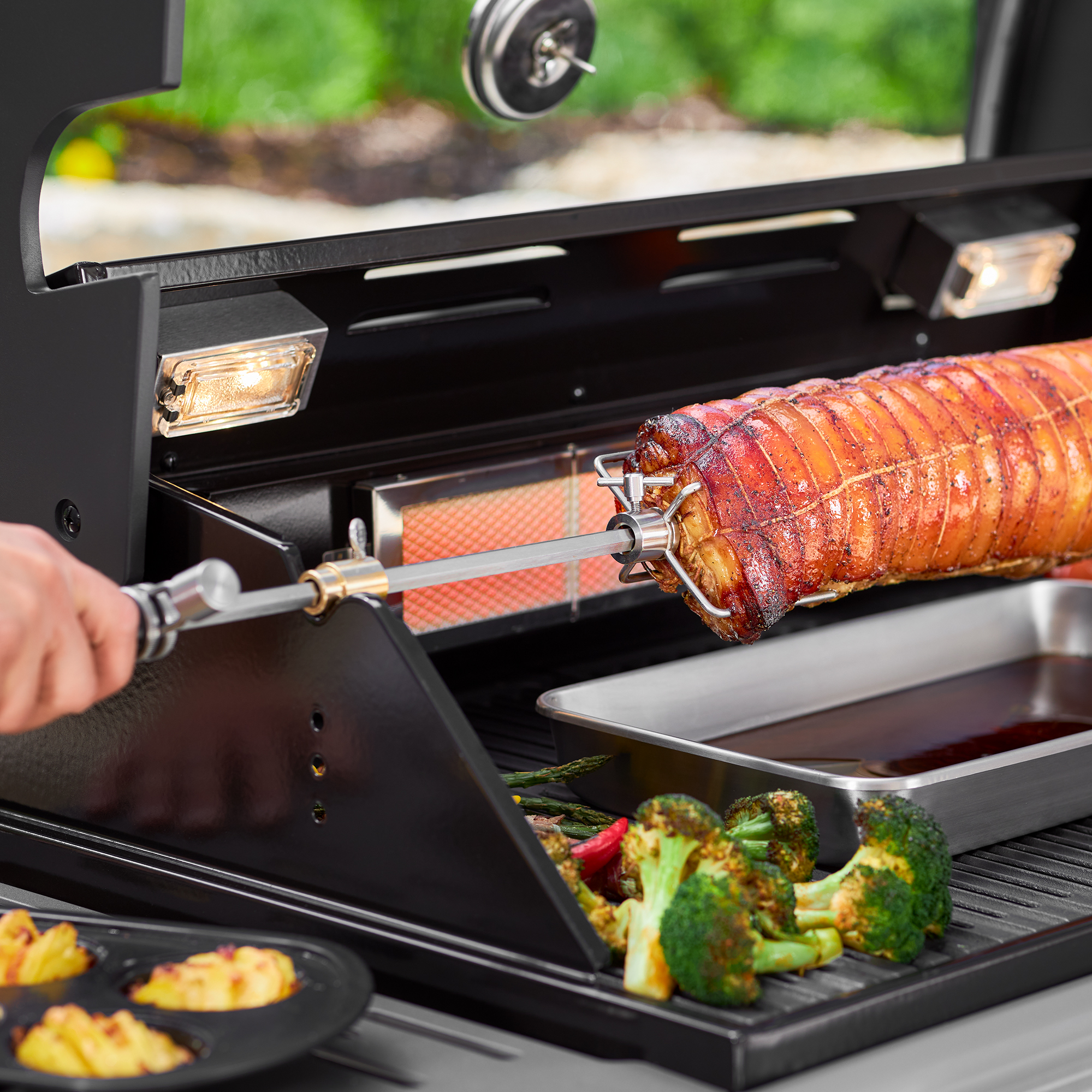 RÖSLE Premium Drehspieß im Einsatz Premium Drehspieß mit einem großen Stück Fleisch, das am Grill rotiert, Gemüse und eine Schale...