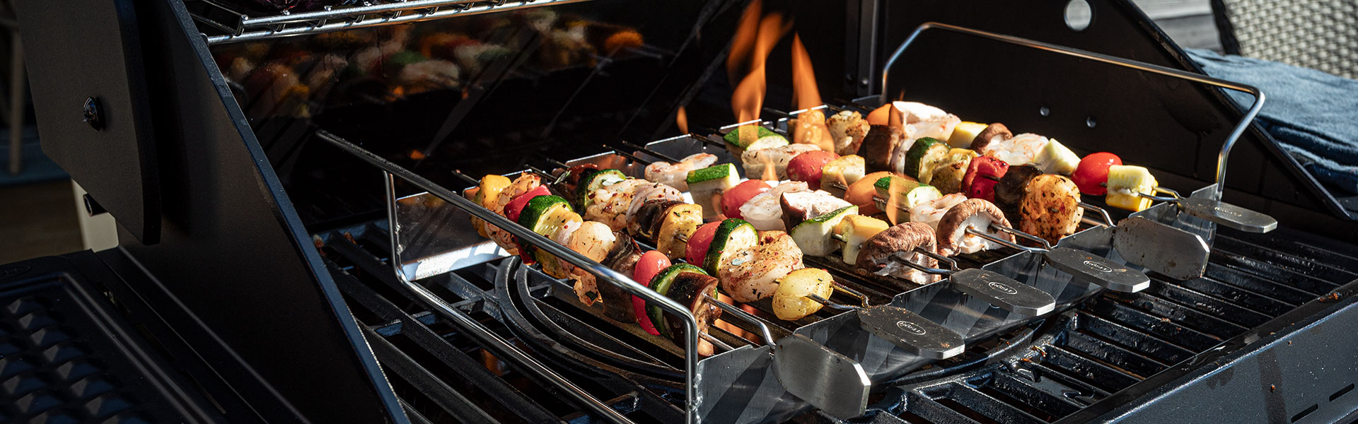 RÖSLE Grillhalter mit Spießen Grillhalter mit Spießen, gefüllt mit Gemüse und Fleischstücken, auf einem Grill mit Flammen...