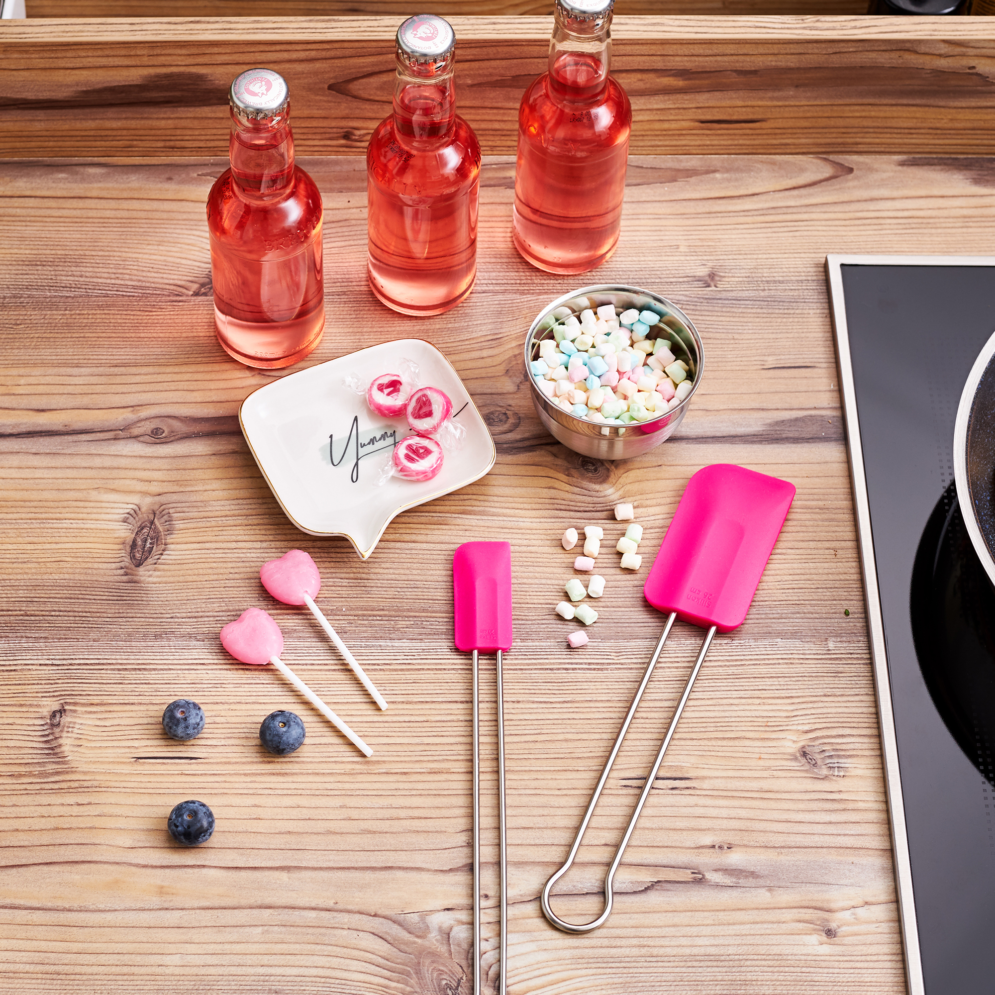 RÖSLE Teigschaber und Süßigkeiten auf einem Tisch Teigschaber in Pink, neben Süßigkeiten und Getränken auf einem Holztisch.