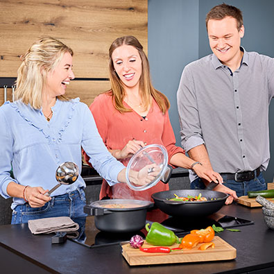 Three friends stand laughing together at the stove and cook together.
