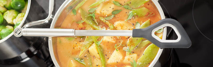 Roestvrijstalen kooklepel met grijs handvat, in een pot met groenten en bouillon.