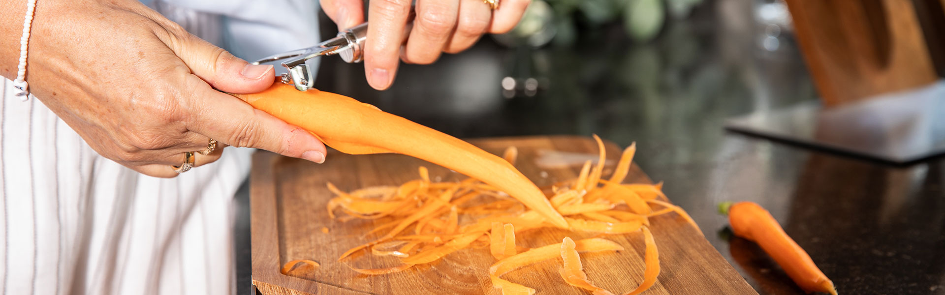 Karotte schälen mit Küchenspezialwerkzeug Eine Person schält eine Karotte mit einem Küchengerät auf einem Holzbrett, Karottenschalen...