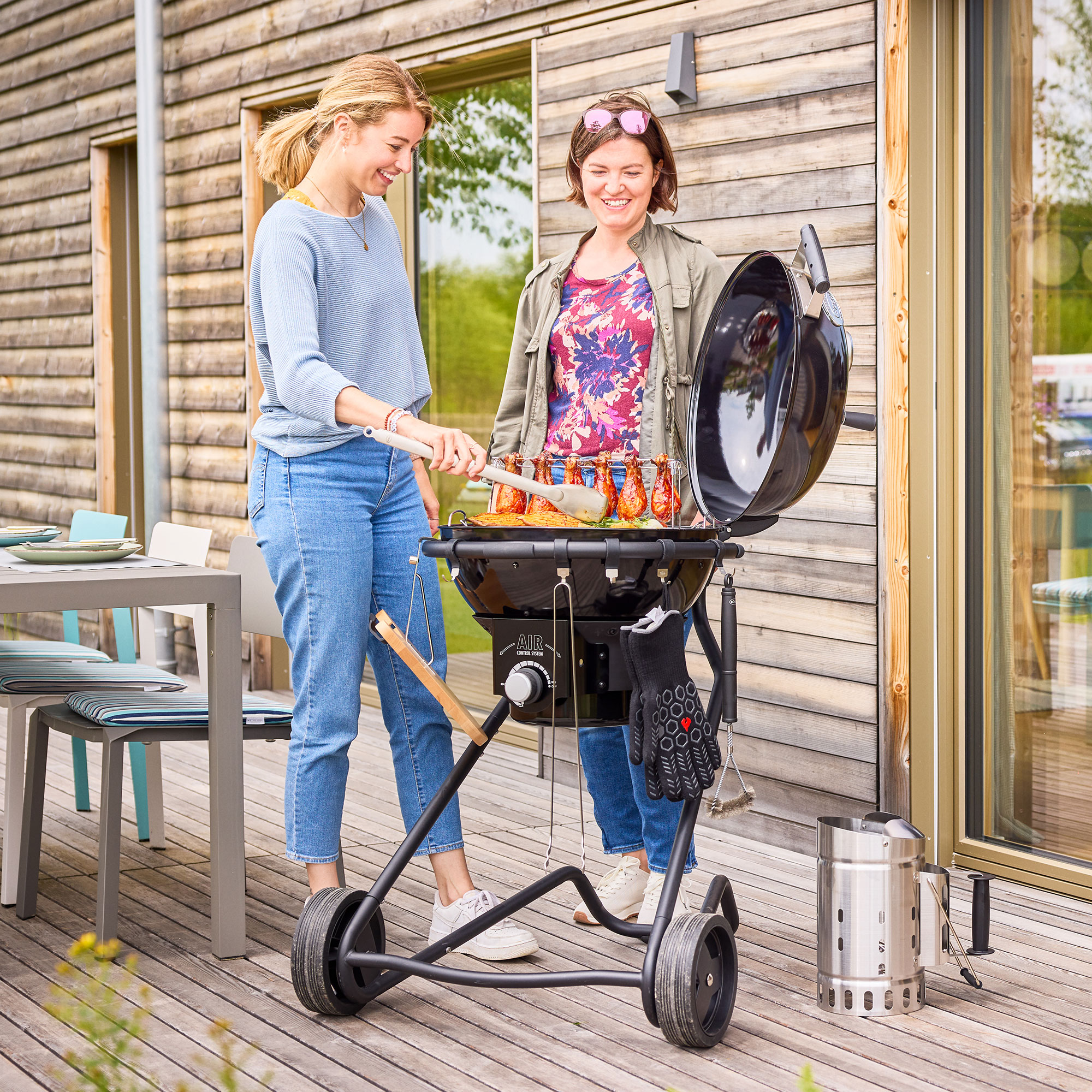 Zwei Frauen beim Grillen mit RÖSLE Holzkohlegrill AIR F50 PRO Zwei Frauen grillen mit dem Holzkohlegrill AIR F50 PRO auf einer Terrasse. Eine Frau hält...