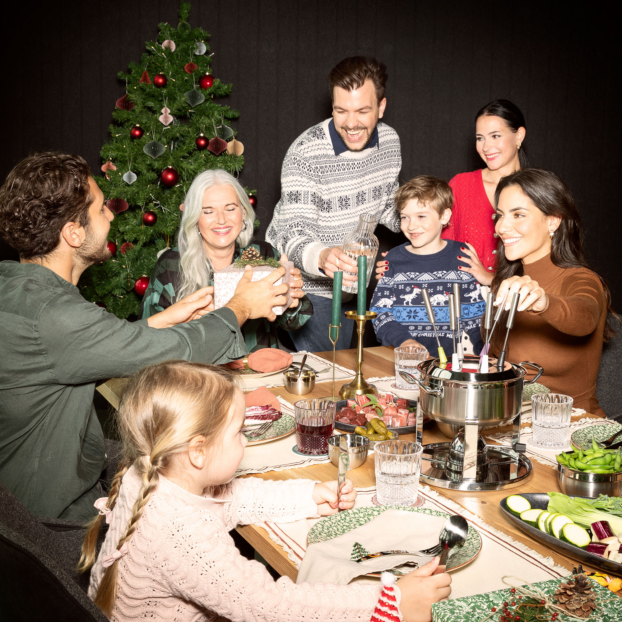 Familienfeier mit Fondue und Weihnachtsbaum Familie sitzt um einen Tisch mit Fondue und feiert zusammen, Weihnachtsbaum im Hintergrund.