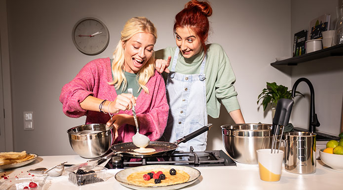 Crepes Zwei Freundinnen machen zusammen Crepes. Frau gießt Teig in die Pfanne