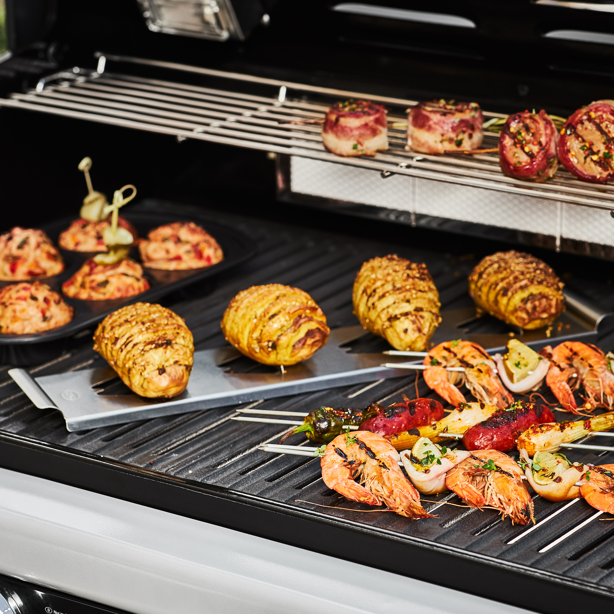 RÖSLE Kartoffelhalter mit Grillgerichten Kartoffelhalter mit gegrillten Kartoffeln, Garnelen und Spießen auf einem Grillrost.