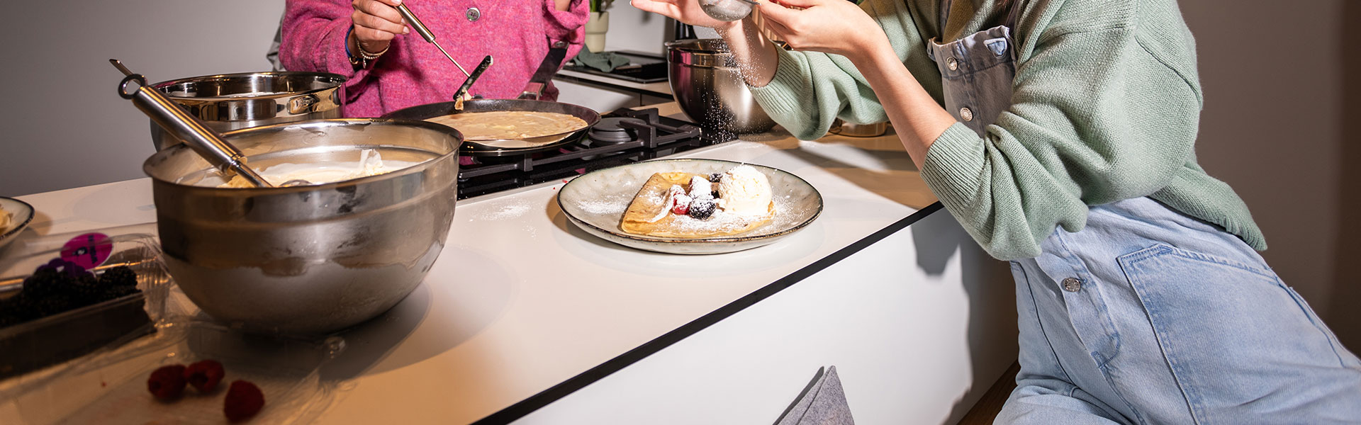 Kitchen scene with pancakes Two people prepare pancakes in a modern kitchen, with bowls and pans on the hob.