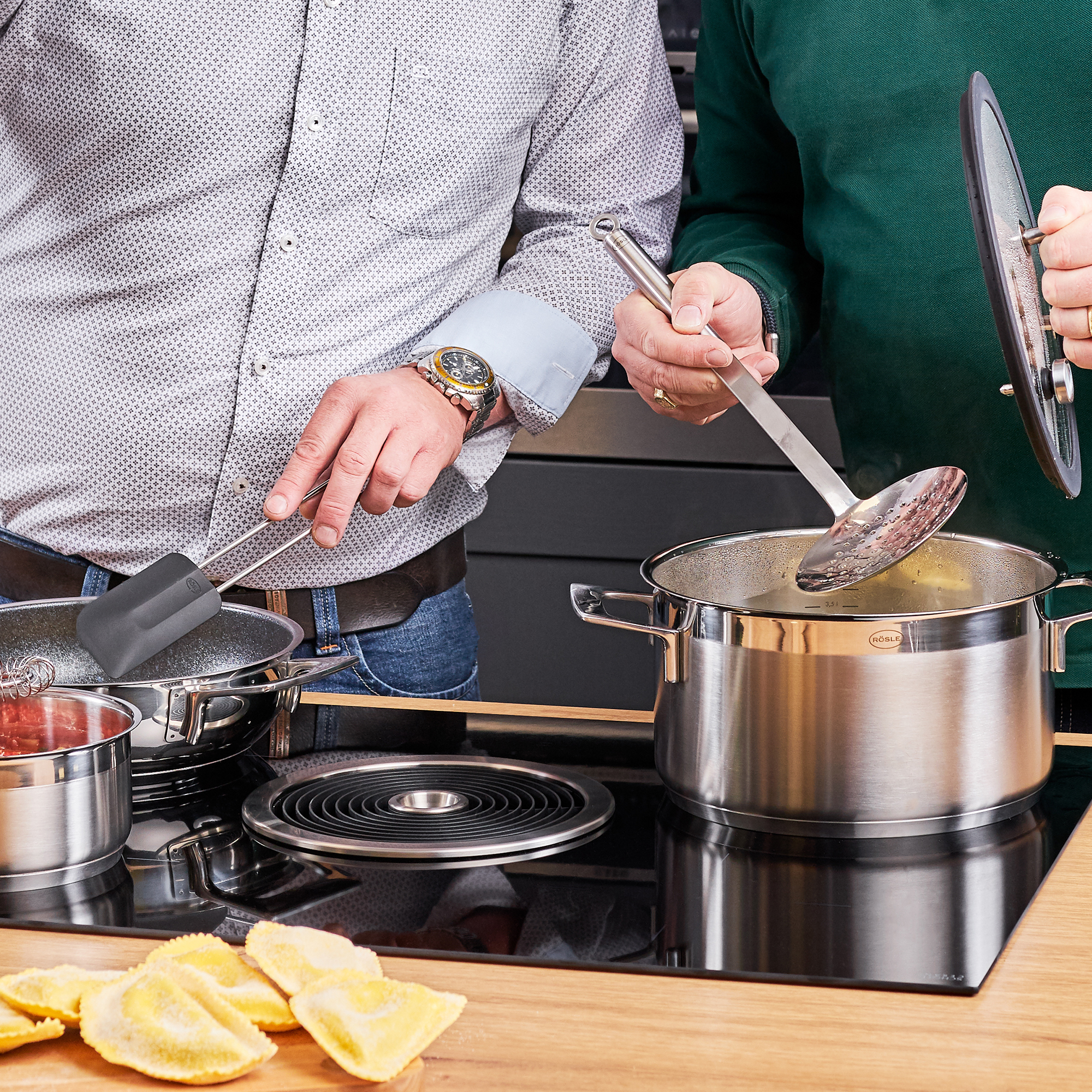 RÖSLE slotted spoon on the hob Skimmer with round handle in action, two people cooking together on the hob.