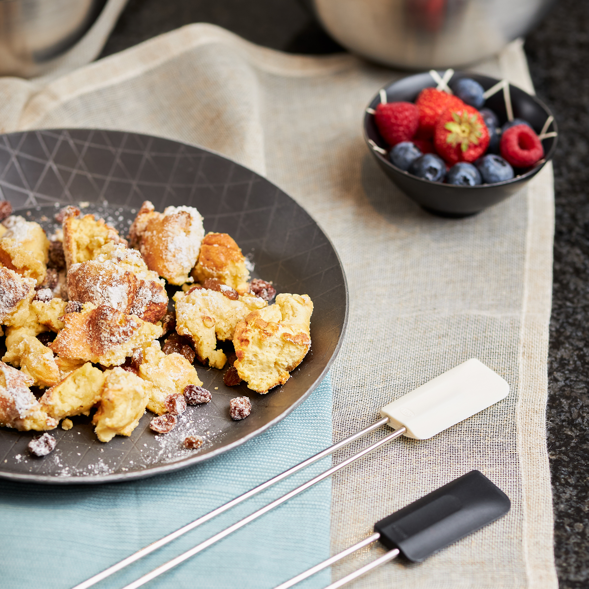 RÖSLE Schmiedeeisen Bratpfanne mit Gebäck Bratpfanne aus Schmiedeeisen mit goldbraunem Gebäck auf einem Teller, umgeben von Beeren und...