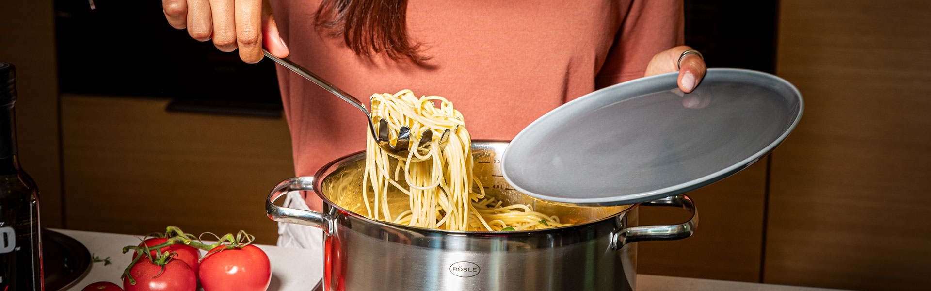 RÖSLE Kochtopf mit Spaghetti Kochtopf aus Edelstahl mit Spaghetti, eine Person hebt die Spaghetti mit einer Zange heraus.