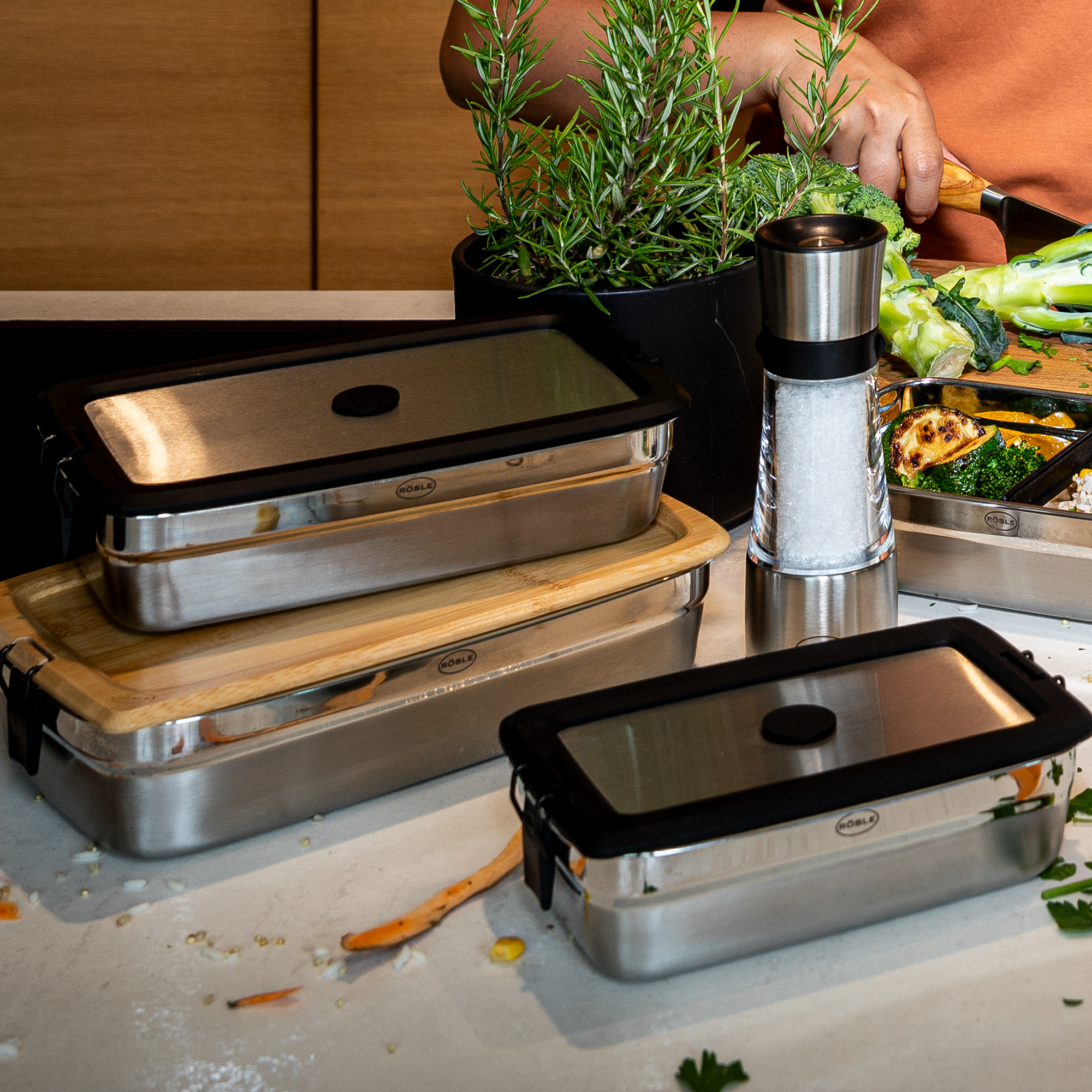 Edelstahlbehälter mit Deckel, stapelbar, in einer modernen Küche, umgeben von frischen Zutaten.