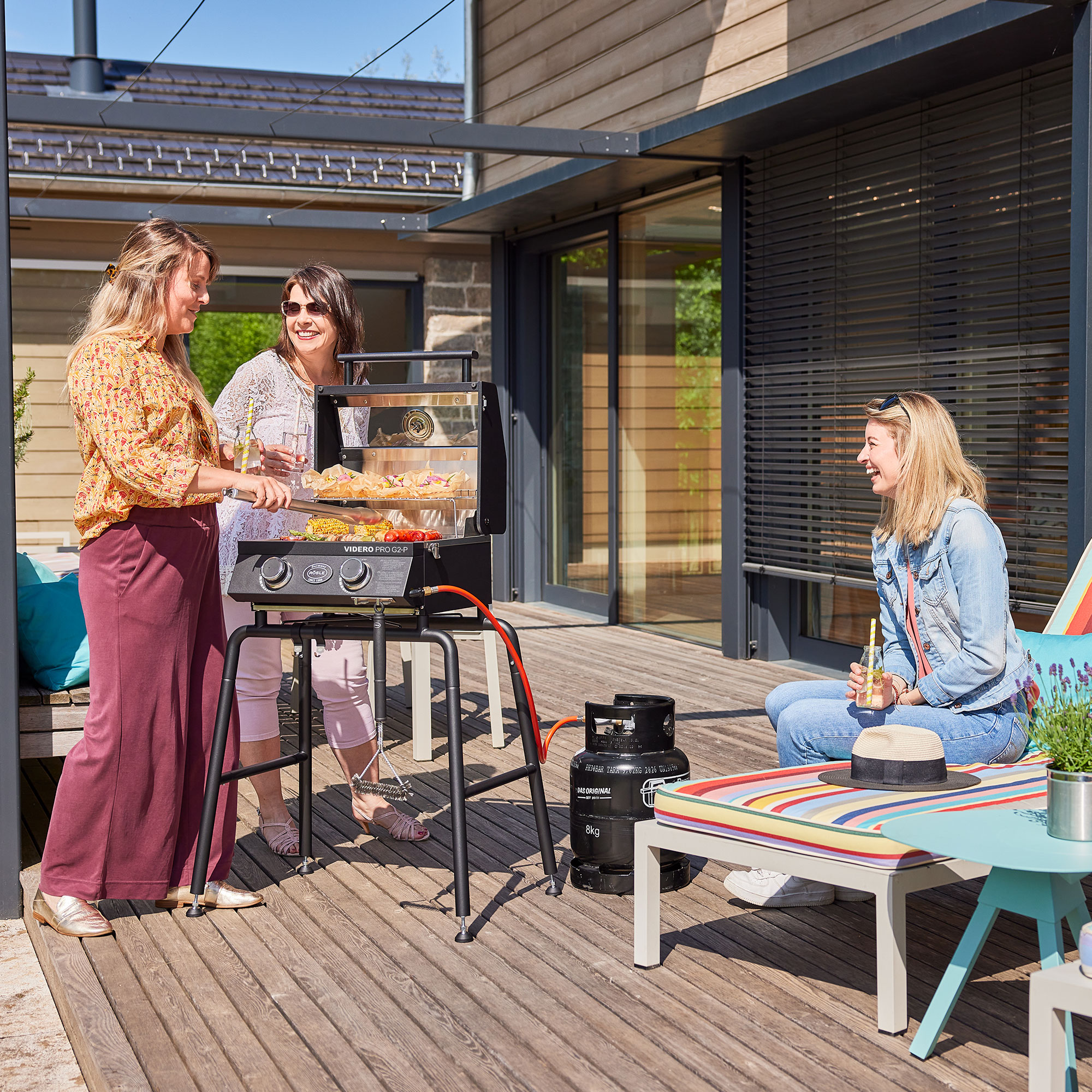 Frauen am Grill auf der Terrasse Drei Frauen stehen um einen Grill auf einer Terrasse, eine grillt, die anderen beobachten...