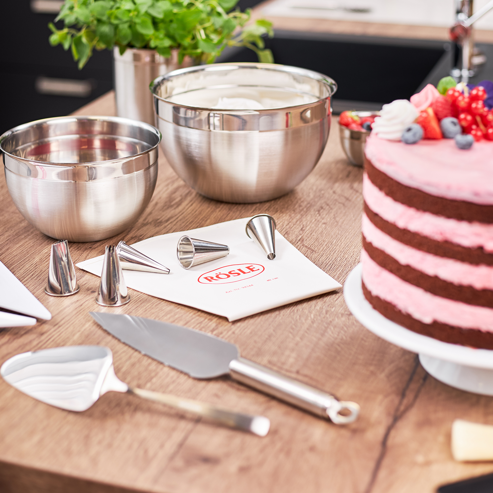 RÖSLE Tortenmesser und Backzubehör Tortenmesser, 30 cm, neben einer mehrschichtigen Torte und Backzubehör auf einem Holztisch.