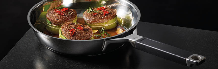 Edelstahlpfanne mit Rindersteaks Edelstahlpfanne mit zwei Rindersteaks und Zucchini, dekoriert mit roten Chilischoten.