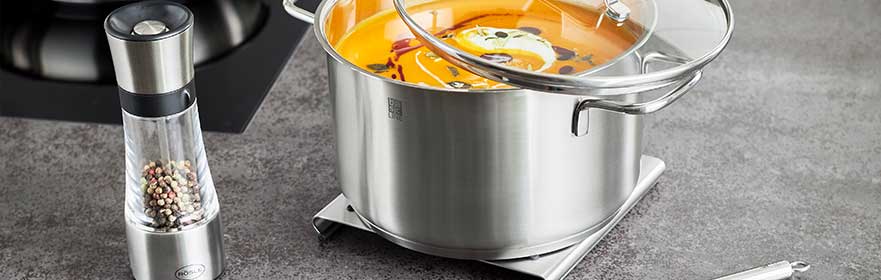 Roestvrijstalen kruidenmolen naast een kookpot met bouillon en groenten.