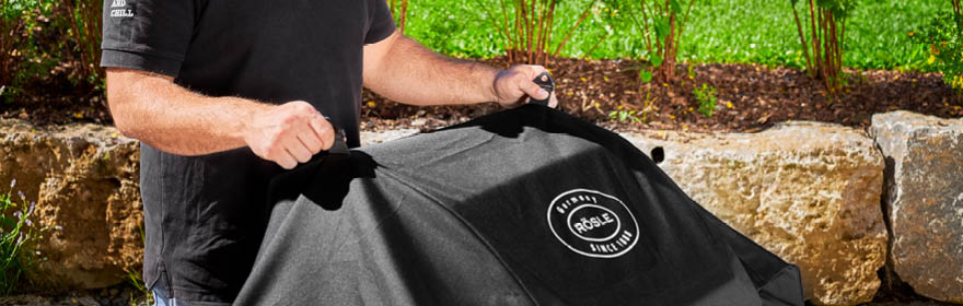 RÖSLE barbecue deksel Grillcover in zwart, wordt door één persoon over een grill getrokken.