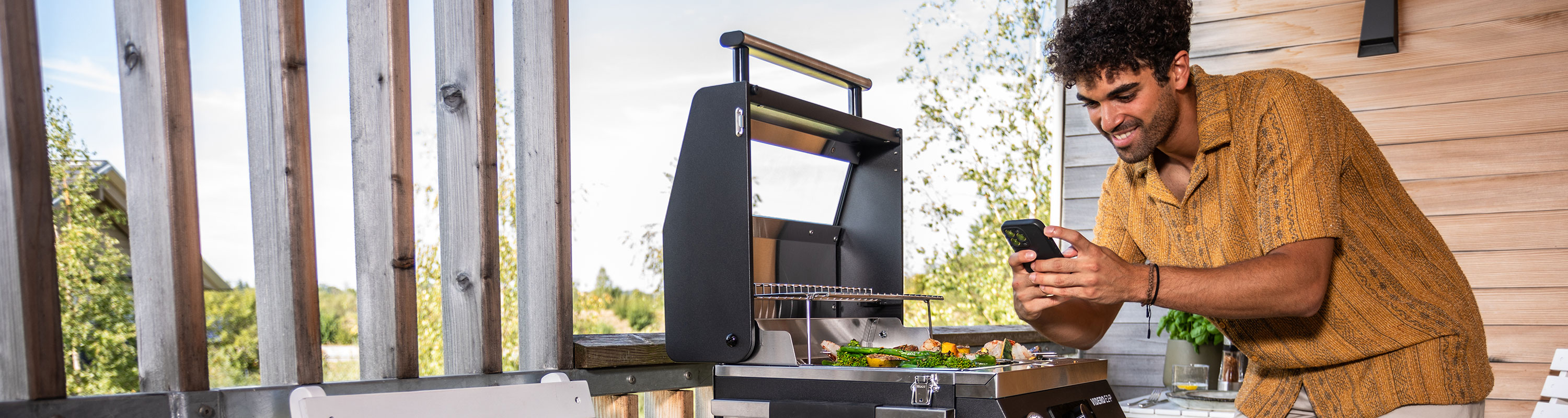 Portable grill Man stands at the barbecue with his mobile phone and takes pictures of the food