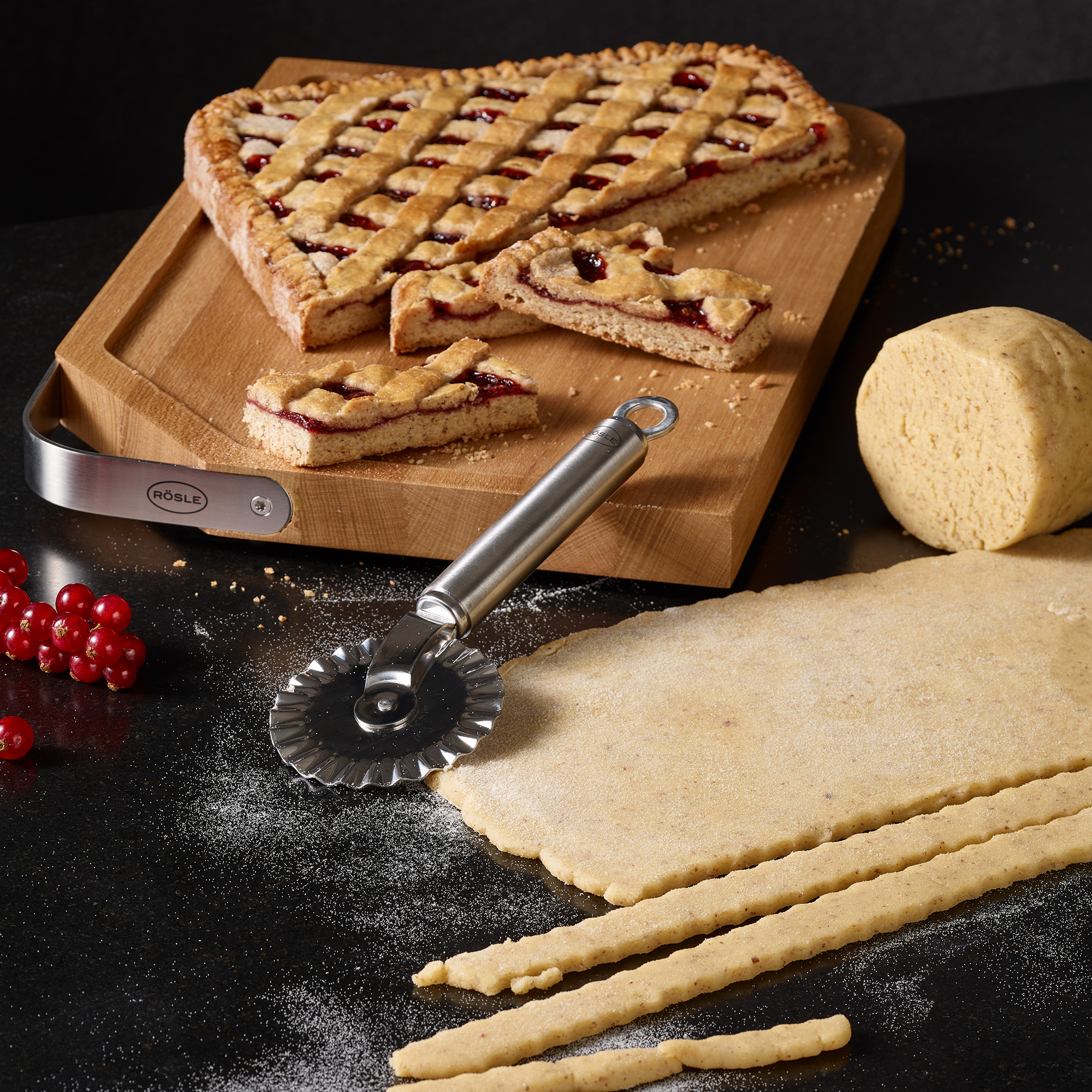 RÖSLE pastries and biscuits on wooden board Pastry wheels on a wooden board with sliced pastry, dough and a stainless steel pizza cutter.