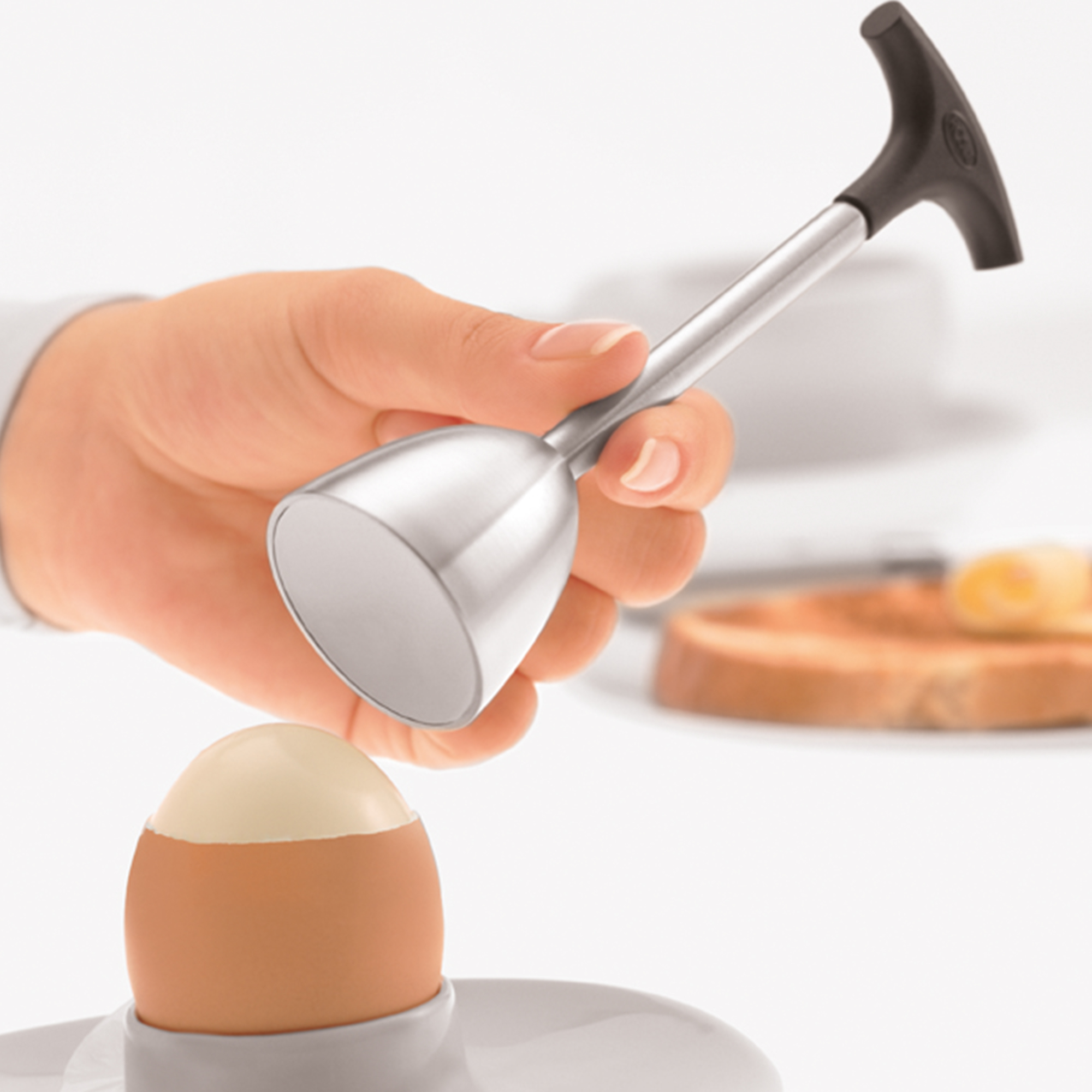 RÖSLE egg beaters Stainless steel egg opener with black handle, held in the hand to open a soft-boiled egg.