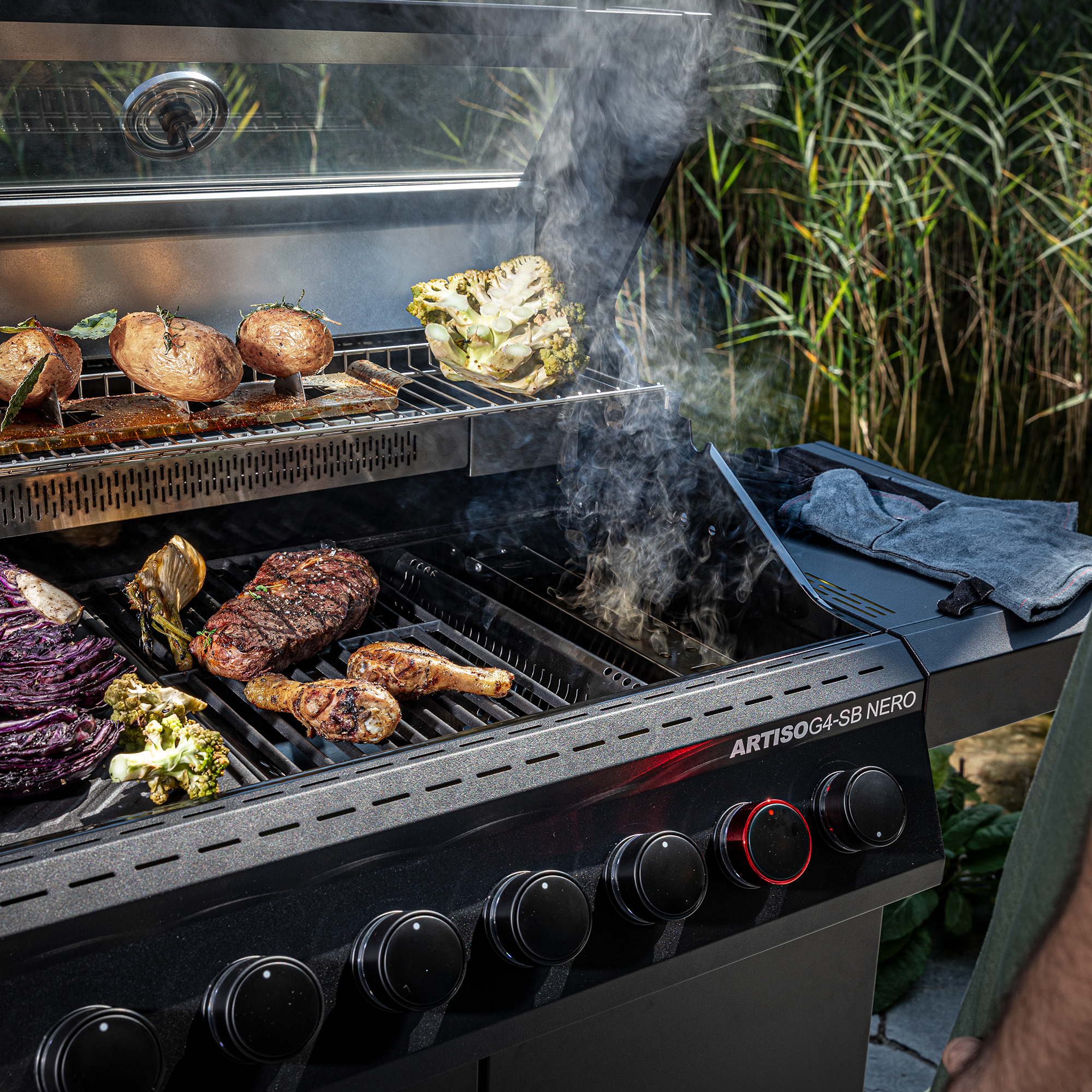 RÖSLE Artiso G4-SB Nero Gasgrill mit Grillgut Artiso G4-SB Nero Gasgrill mit Gemüse und Fleisch auf dem Grillrost, Rauchentwicklung sichtbar.