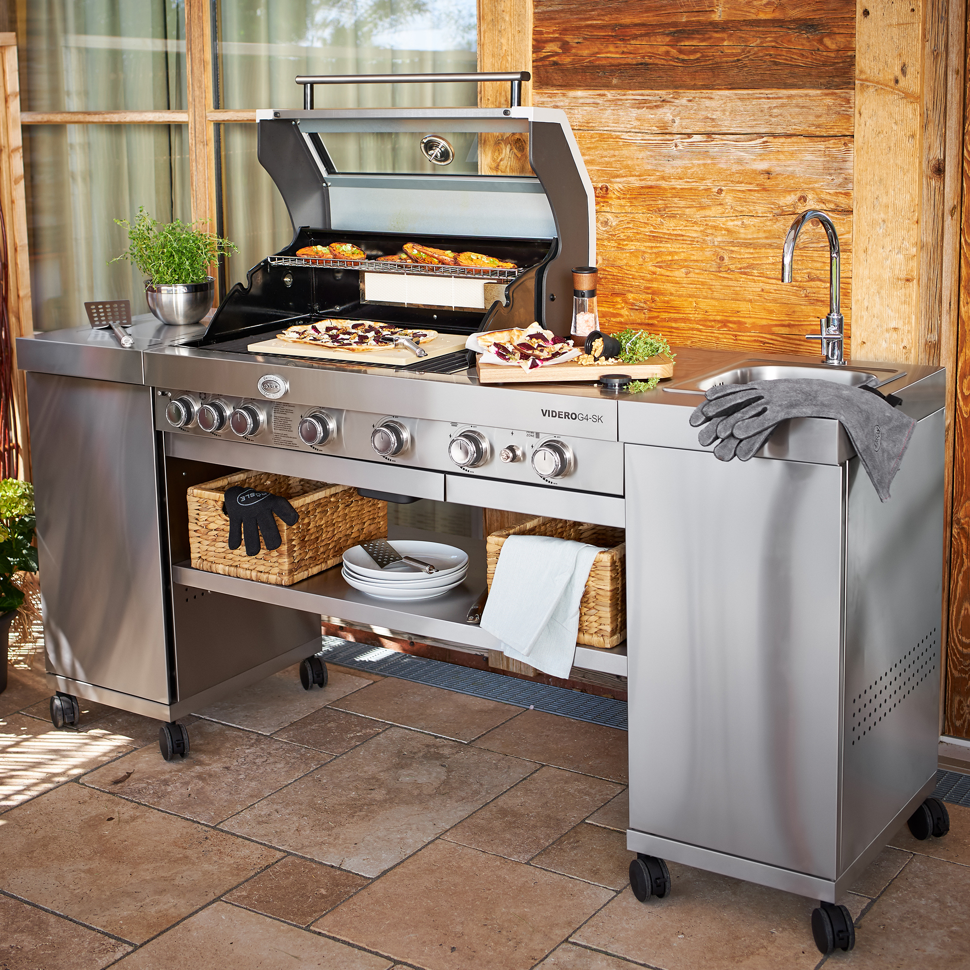 Gasgrill Videro G4-SK Vario aus Edelstahl mit offener Haube, Grillfläche und seitlichem Waschbecken.
