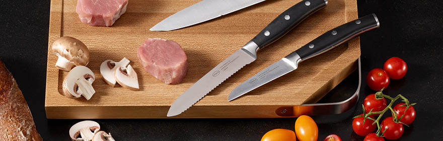 Keukenmessenset van RÖSLE Keukenmes op een houten plank met vlees, champignons en tomaten.