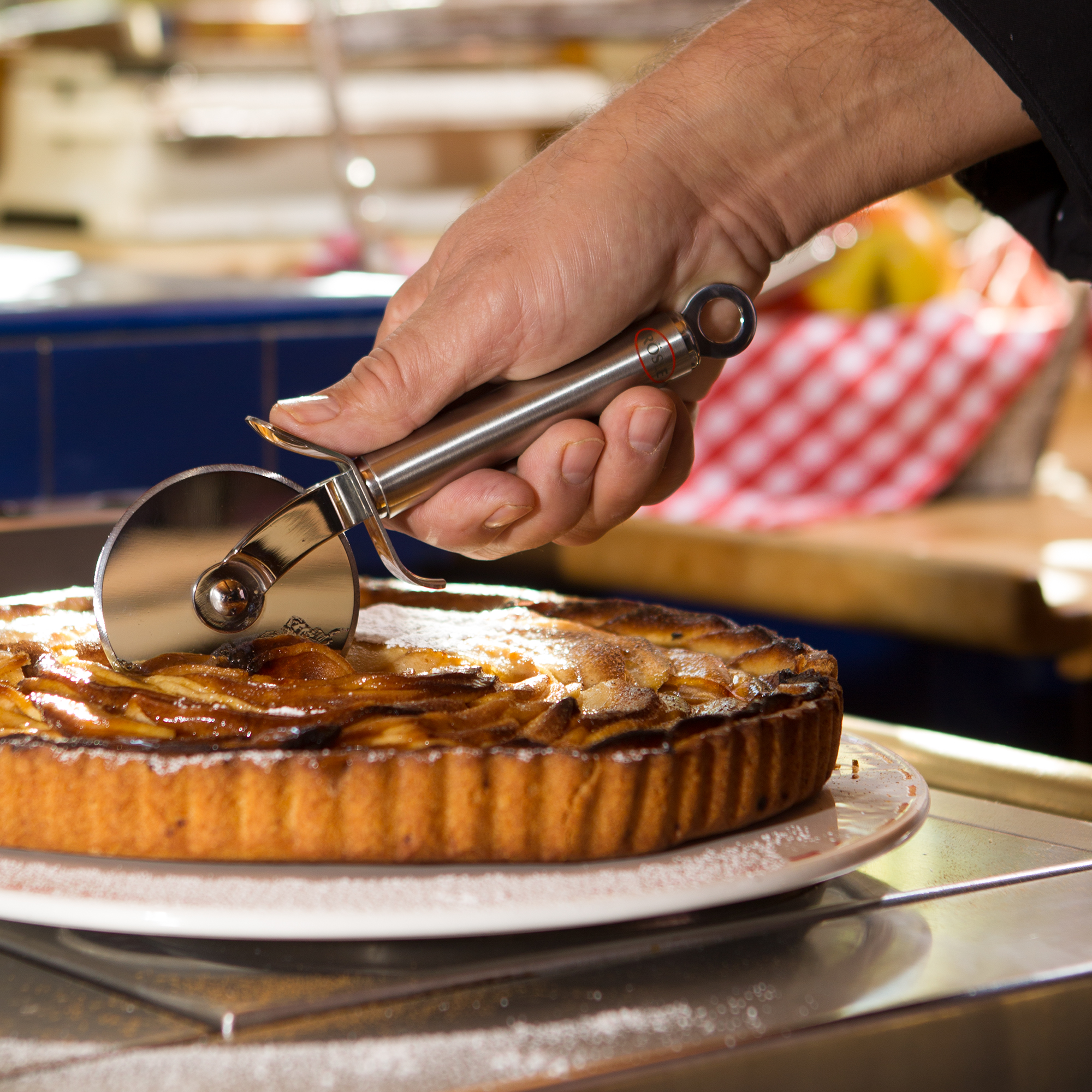RÖSLE pizza and tarte flambée cutter Stainless steel pizza and tarte flambée cutter, in the hands of a chef, cuts an apple pie.