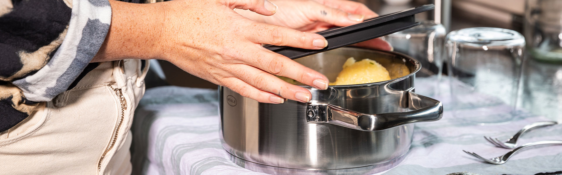 RÖSLE Bratentopf mit Deckel Bratentopf aus Edelstahl mit Deckel, eine Person hebt den Deckel an, um den Inhalt zu überprüfen.