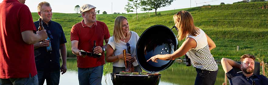Barbecue accessories Sport series Group of six people barbecuing by the lake, with barbecue and drinks, outdoors in daylight.