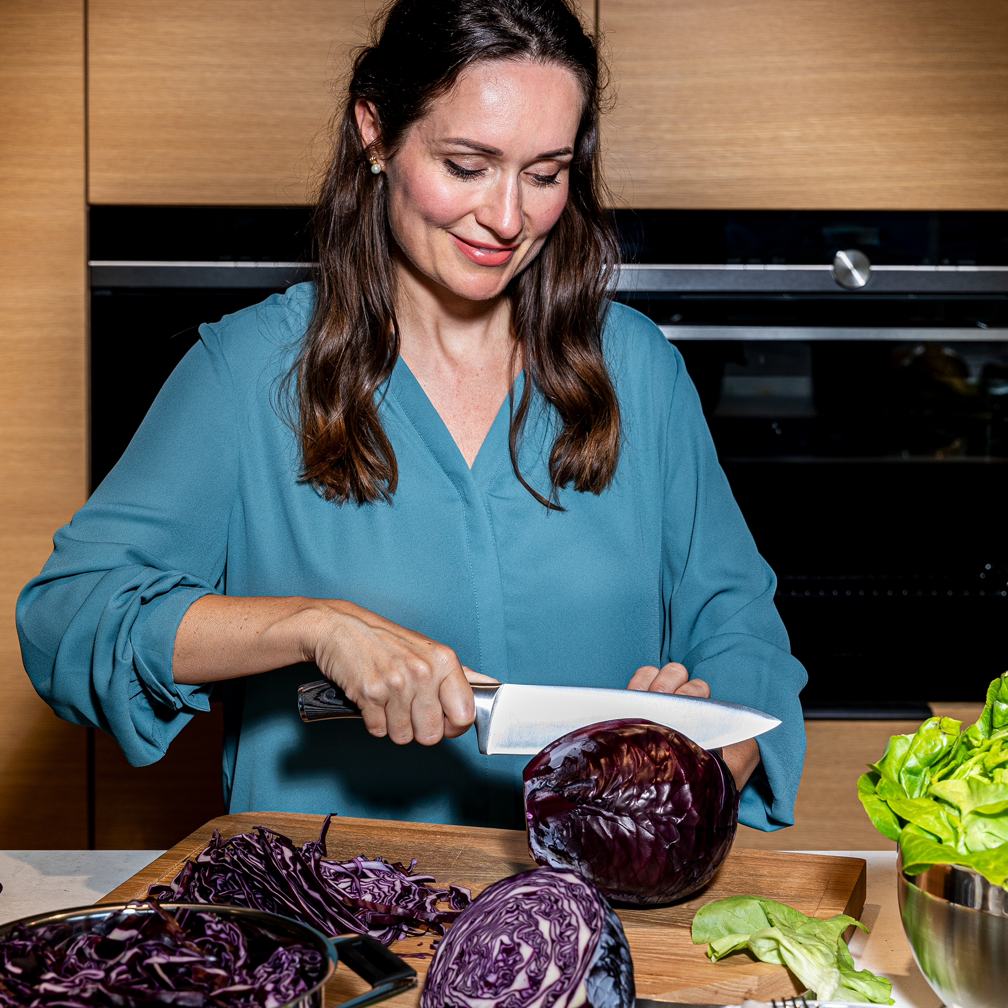 Frau schneidet roten Kohl mit RÖSLE Kochmesser Kochmesser in Verwendung, eine Frau schneidet roten Kohl auf einem Holzbrett.