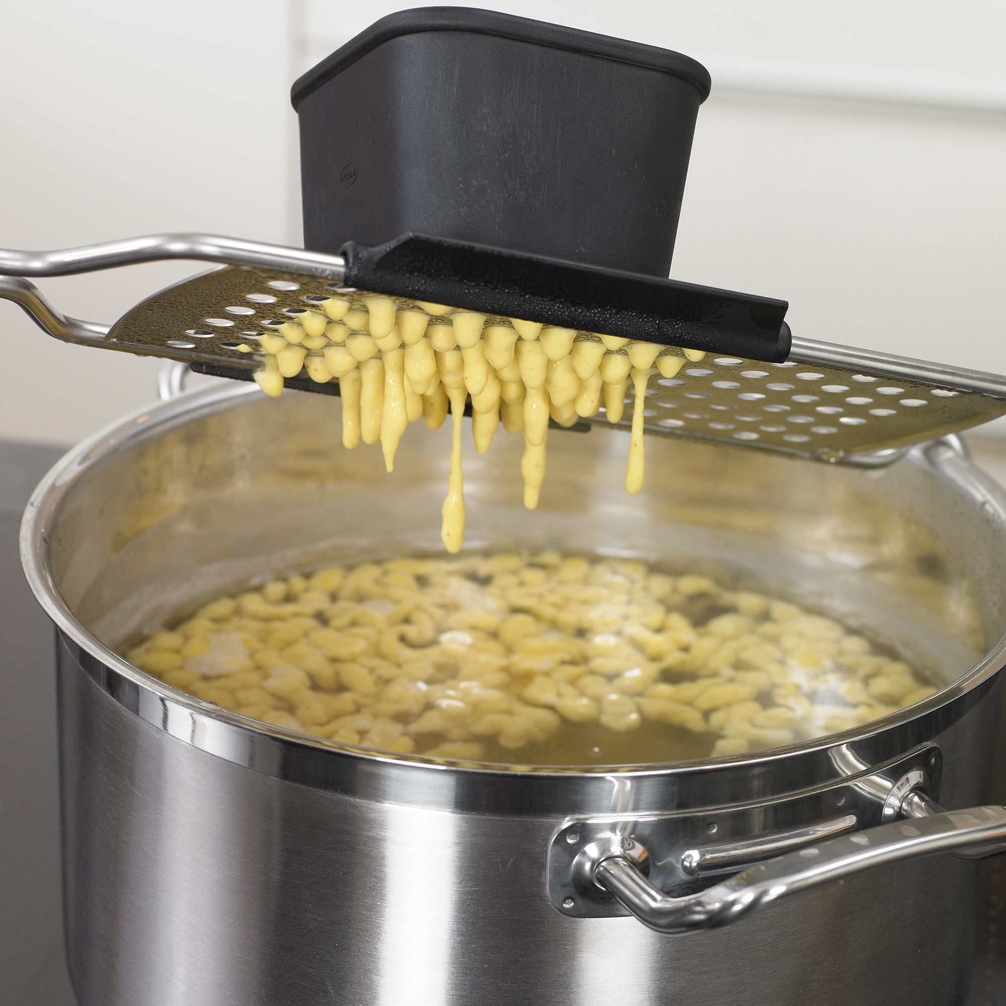 RÖSLE spaetzle slicer over a pot Stainless steel spaetzle slicer with black container, over a pot of boiling water, spaetzle...