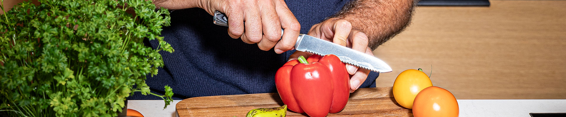 RÖSLE Küchenmesser mit roter Paprika Küchenmesser in der Hand, das eine rote Paprika auf einem Holzbrett schneidet.