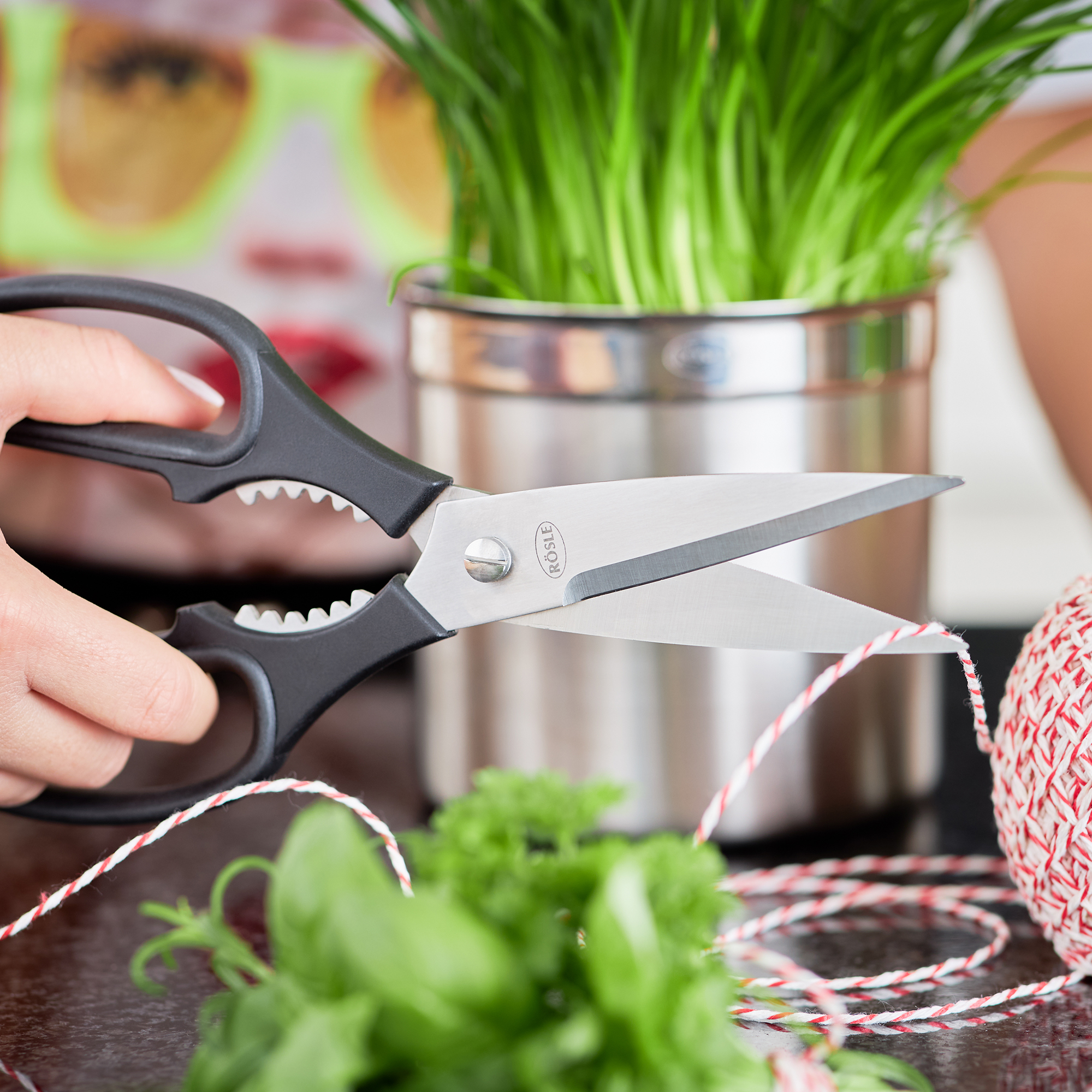 RÖSLE kitchen shears in action Kitchen scissors with black handle, cutting herbs and string, fresh herbs in the foreground...