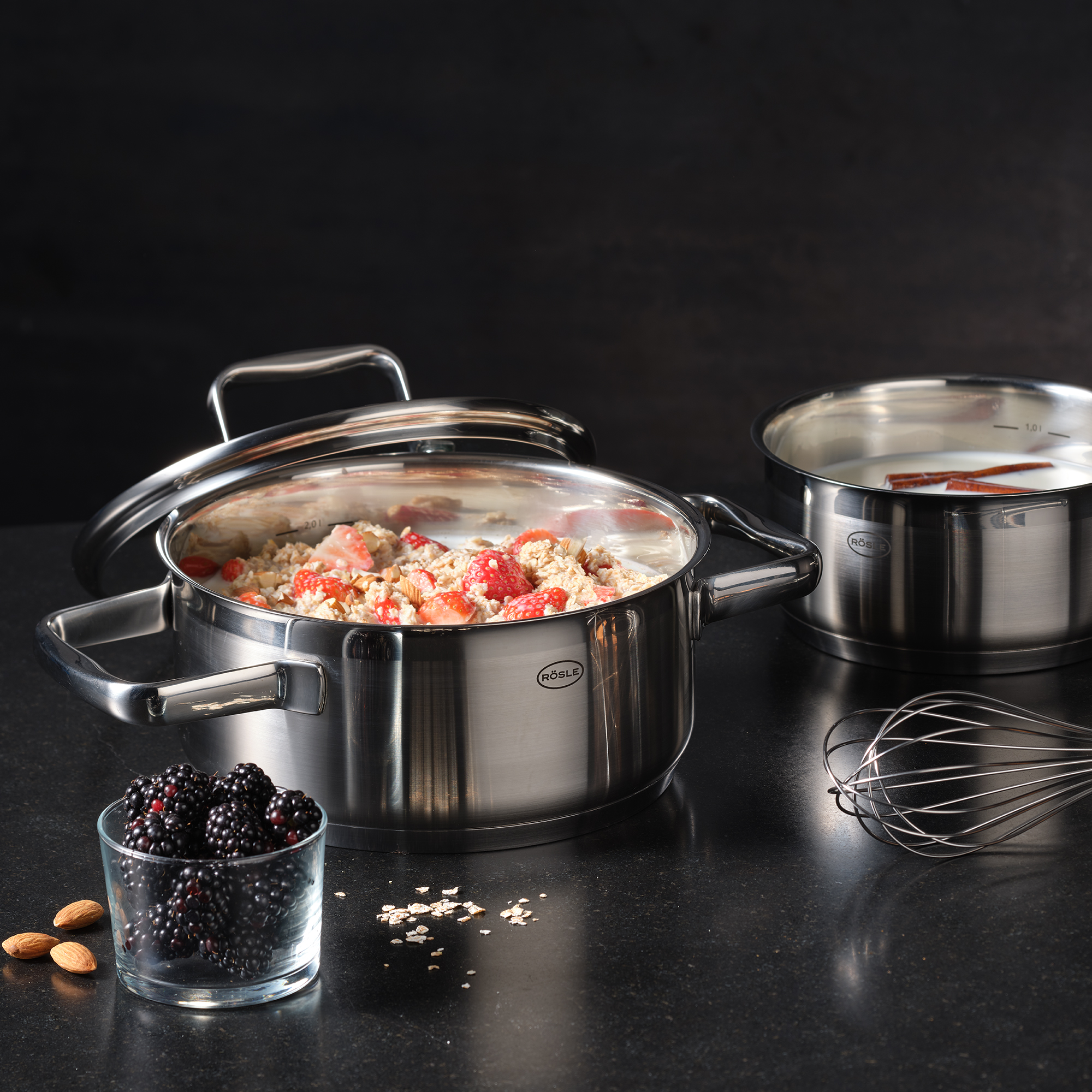 Roasting pan, 20 cm, made of stainless steel, filled with vegetables and fruit, next to it a bowl with berries and a whisk.