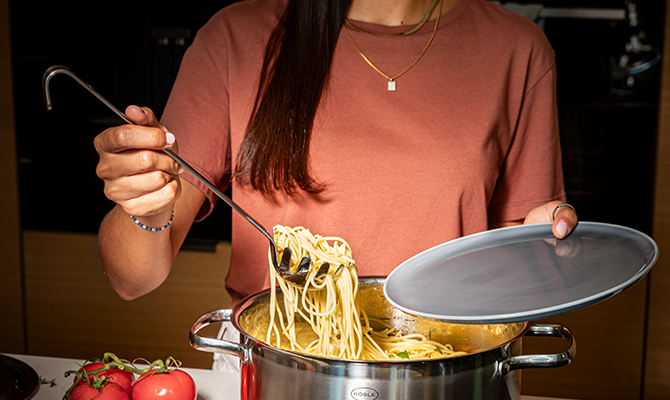 Rezepte Kochen Frau holt mit dem Spaghettiheber Spaghettis aus dem Topf auf einen Teller.